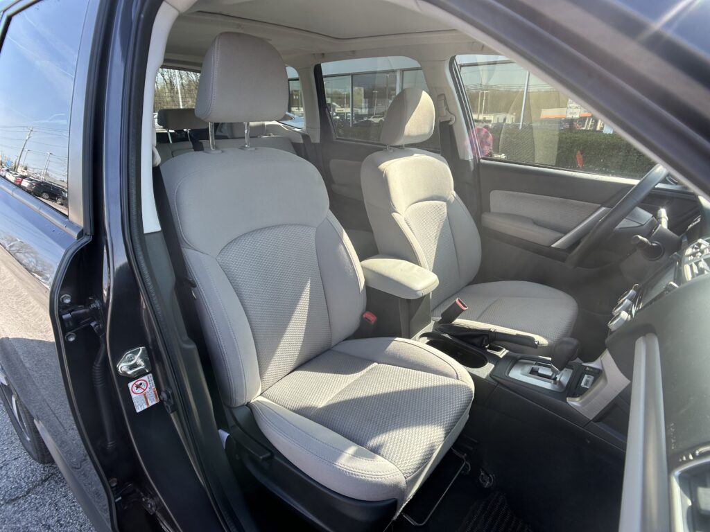 Interior of a car with gray cloth front seats, center console, and steering wheel; driver’s door open.