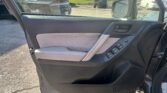 Driver-side car door panel with window controls and armrest; parking lot visible through the open door window and mirror behind.