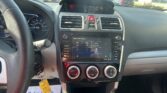 Interior of a car dashboard with a touchscreen infotainment system, circular climate controls, and steering wheel on the left, parked in a lot.
