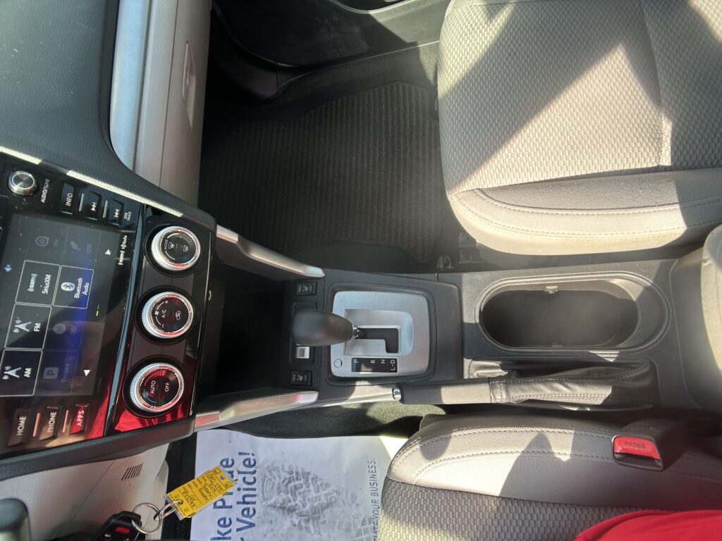 Interior of a car focusing on the center console: touchscreen, climate controls, gear selector, and front passenger seat with patterned fabric.