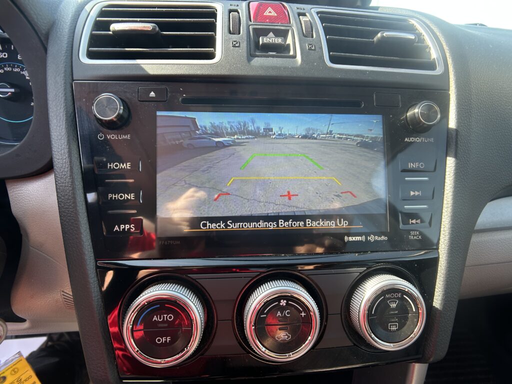 Car infotainment screen showing rearview camera with parking guidelines and text 'Check Surroundings Before Backing Up' for backing up safety.