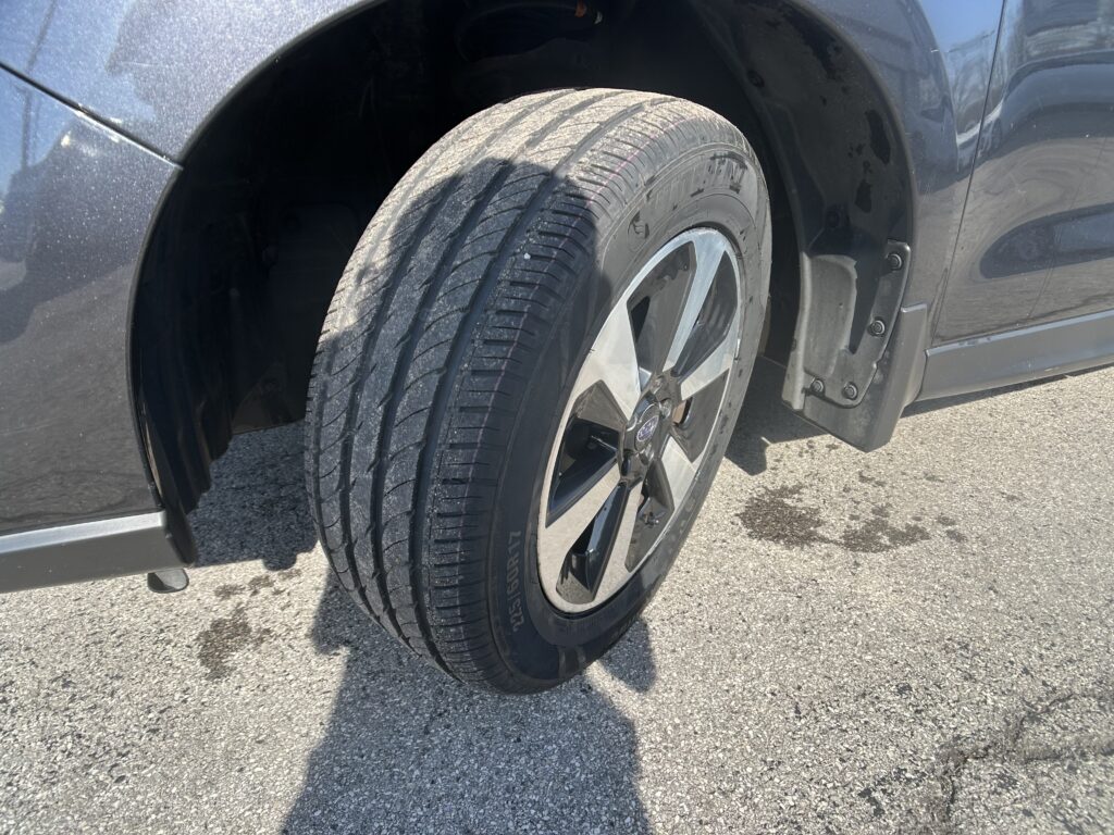 Close-up of a car tire and alloy wheel in a wheel well of a dark blue vehicle.