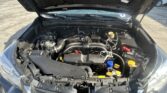 Front view of a car with the hood open, showing the engine bay and various hoses, wires, and components including the battery and yellow oil dipstick.