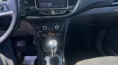 Interior view of a car dashboard: steering wheel on left, central touchscreen shows a warning message, gear shifter and cup holders in foreground.