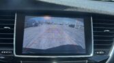 Car dashboard display showing the rearview camera feed with orange guiding lines over a parking lot scene