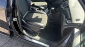 Open driver's door view of a black car interior showing front seats, center console with gear shifter, and steering wheel.