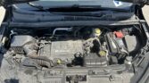 Open hood reveals engine bay of a Buick car with various hoses, battery, and coolant reservoir visible under the hood.