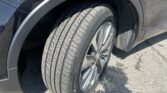 Close-up of a car wheel and tire in the wheel arch of a black vehicle, showing the silver trim and reflections on the body.