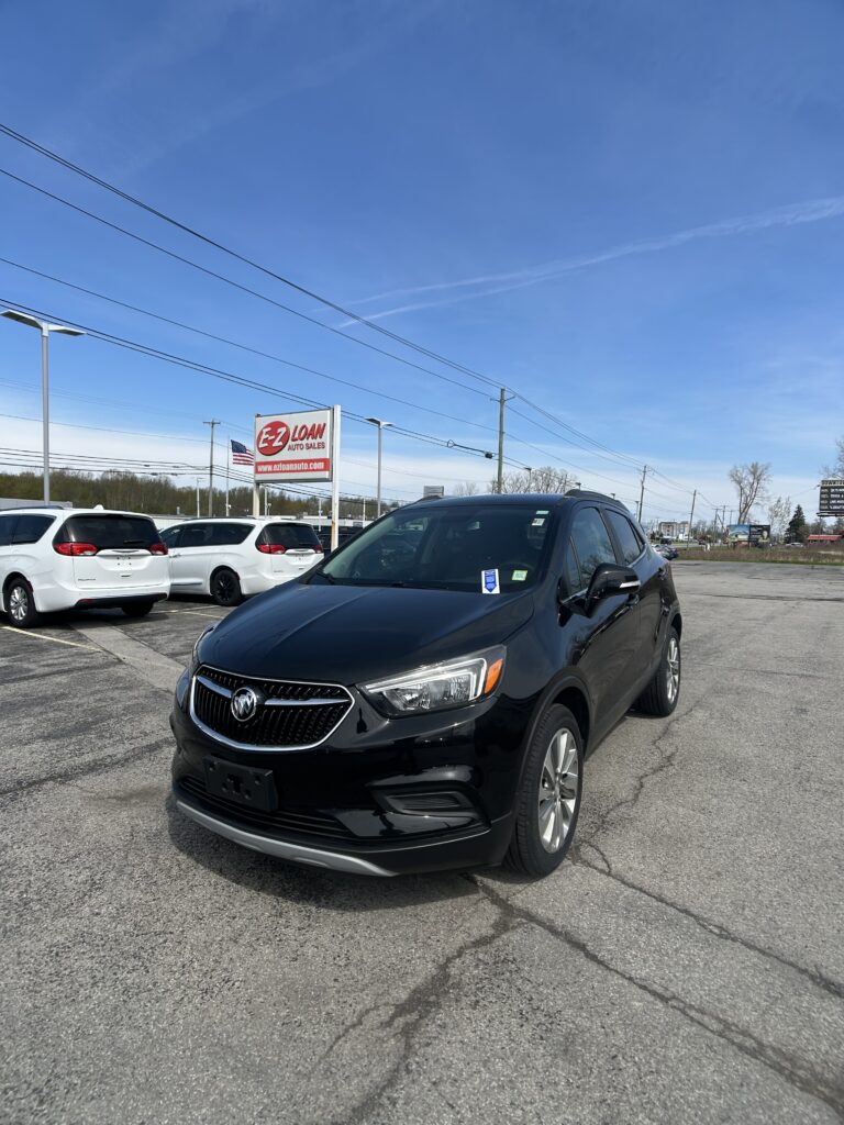 Black Buick SUV in a car dealership lot with EZ Loan Auto Sales sign and other white vehicles nearby under a clear blue sky.