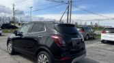 Black Buick SUV in a parking lot with tall utility poles and overhead power lines against a blue sky.