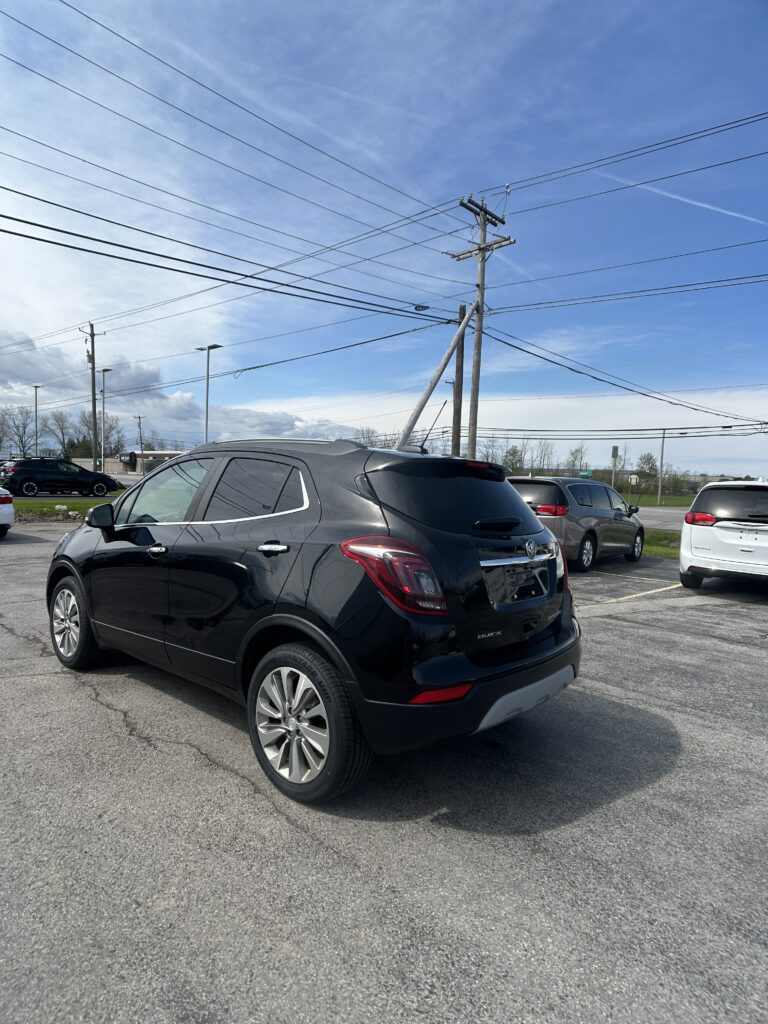 Black Buick SUV in a parking lot with tall utility poles and overhead power lines against a blue sky.