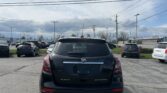Rear view of a black Buick Encore in a car dealership lot with other vehicles visible in the background under a cloudy sky.