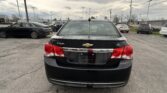 Rear view of a black Chevrolet Cruze LT in a dealership parking lot with other cars and power lines overhead.