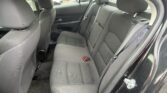 Rear passenger seating area inside a dark cloth-fabric car, three-seat bench with headrests and visible seatbelts, windows showing parked cars outside