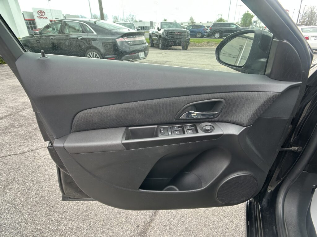Interior of a car door panel with power window controls, view of a dealership parking lot outside the window