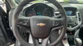 Close-up of a Chevrolet steering wheel and instrument cluster inside a car, with a parking lot visible through the windshield.