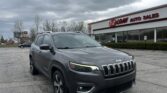 Gray Jeep SUV in the parking lot of EZ Loan Auto Sales with a cloudy sky above and the dealership building in the background.