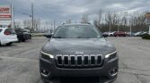 Front view of a gray Jeep SUV parked in a dealership lot under a cloudy sky.