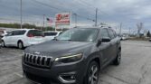 Gray Jeep SUV in a car lot with an E-Z Loan Auto Sales sign in the background and an American flag nearby