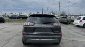 Rear view of a gray Jeep SUV in a parking lot with other cars and cloudy sky above.
