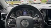 View from the driver's seat in a Jeep, showing the steering wheel and instrument cluster with a parking lot outside.