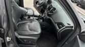 Interior of a dark leather SUV with the driver’s door open, showing the steering wheel, center console, and front seats.