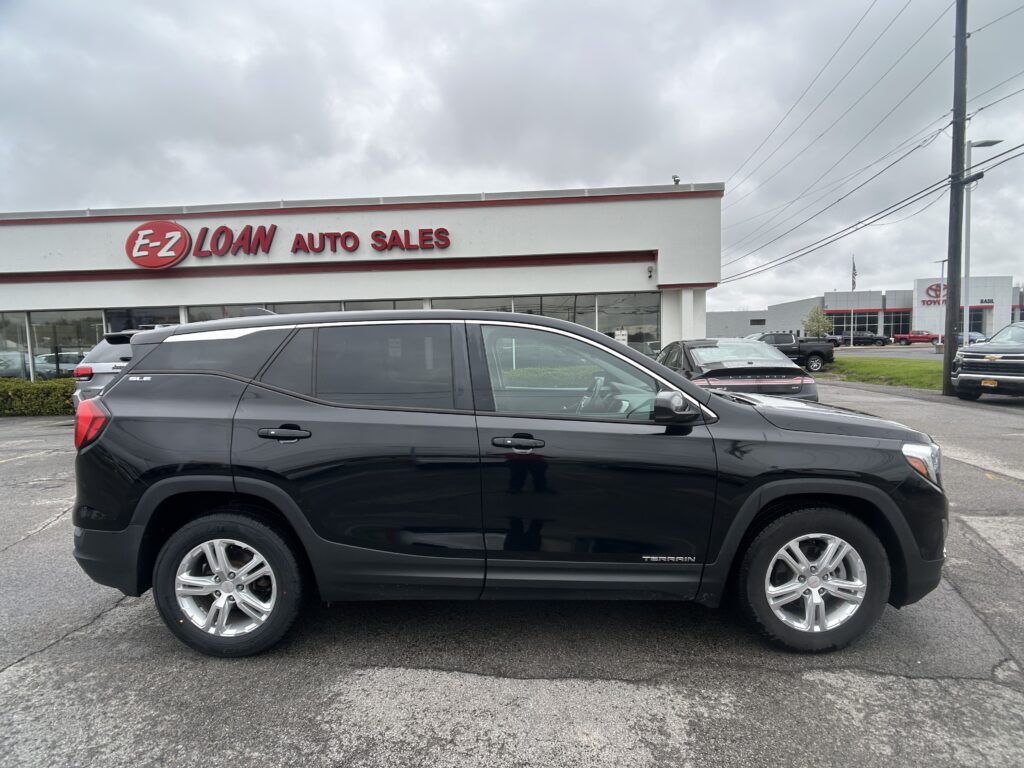 Dark gray GMC Terrain SUV parked in front of EZ Loan Auto Sales building on a cloudy day, dealership sign visible in background.