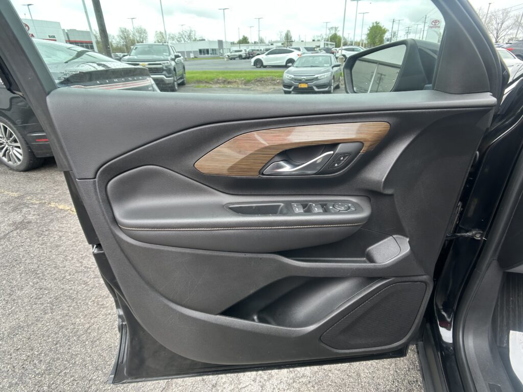 Inside of a car door panel with black plastic, wood grain trim, and a silver door handle; window and lock controls visible on the armrest area.