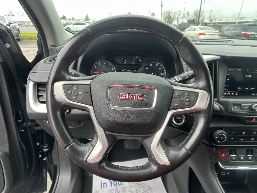 View from the driver's seat showing a GMC steering wheel, instrument cluster, and center console with a touchscreen display to the right, parked interior.