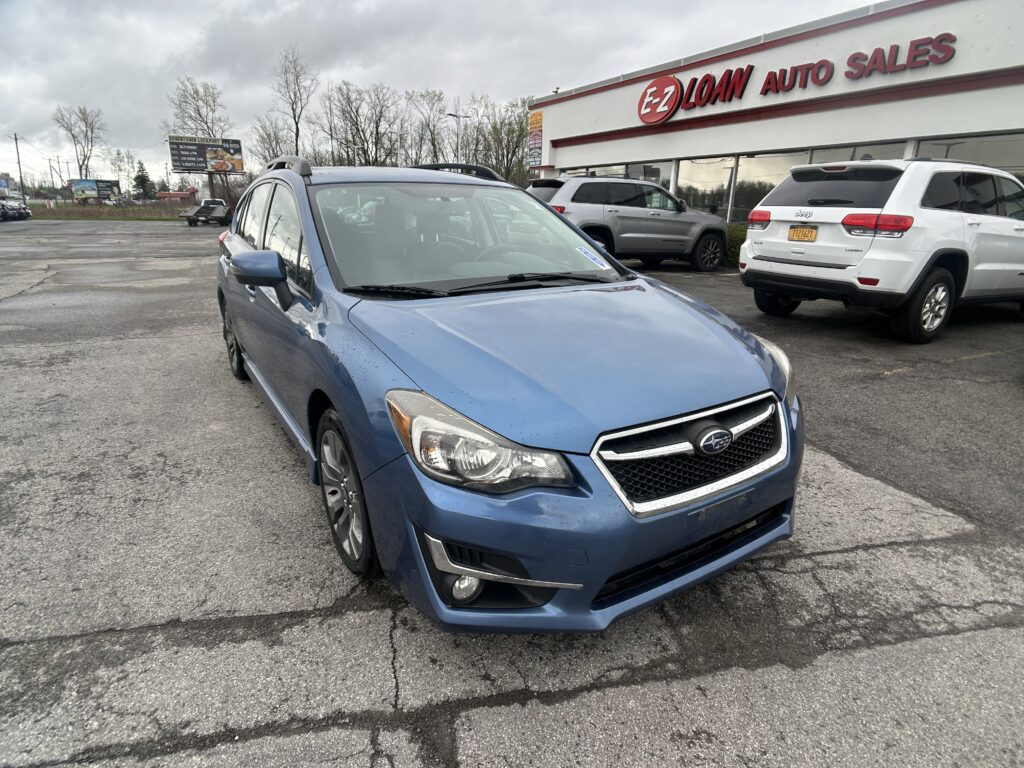 Blue Subaru SUV in a dealership lot with an E-Z Loan Auto Sales storefront and other cars in the background under a cloudy sky.