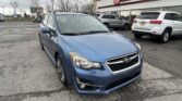 Blue Subaru SUV in a dealership lot with an E-Z Loan Auto Sales storefront and other cars in the background under a cloudy sky.