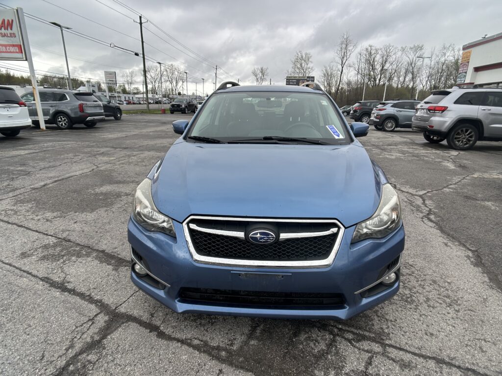 Front view of a blue Subaru SUV in a crowded car lot on a cloudy day, with other vehicles in the background