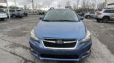 Front view of a blue Subaru SUV in a crowded car lot on a cloudy day, with other vehicles in the background