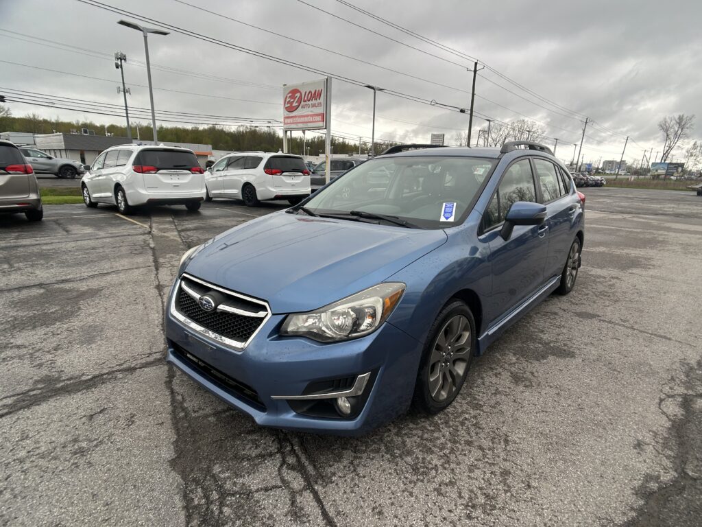 Blue SUV in the foreground at a car dealership lot with white minivans parked behind and an E-Z Loan sign visible in the background on a cloudy day.