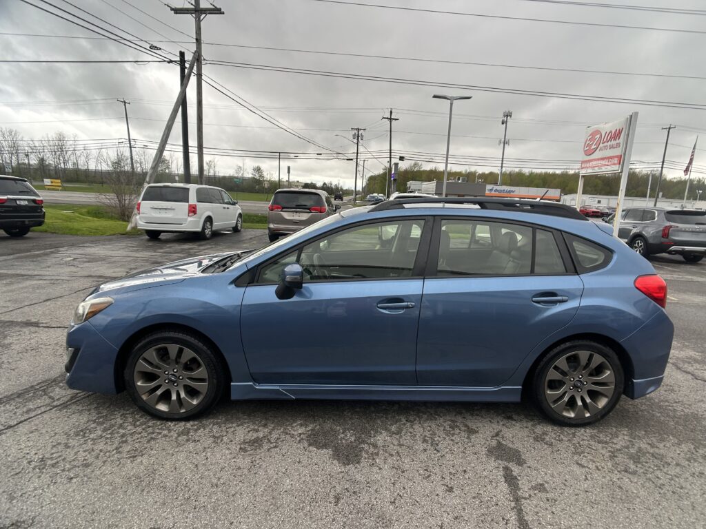 Blue sedan in foreground parked in a lot with several other cars and a cloudy sky, utility poles and power lines overhead.