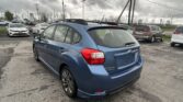 Blue Subaru SUV in foreground, parked in a busy dealership lot on a gray, cloudy day with power lines overhead.
