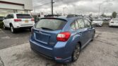 Blue Subaru Impreza parked in the foreground at a car dealership lot, with other cars and a Toyota dealership building in the background.