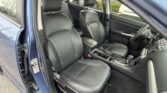 Blue car interior with black leather front seats, headrests, and center console visible; steering wheel on the right side and door panel in view.