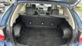 Open tailgate of a blue SUV revealing a spacious cargo area with folded rear seats and a rubber cargo mat in a parking lot, blue sky visible.