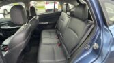 Dark leather back seat area of a sedan with two headrests, middle seat, and seat belts; view through side windows of parked cars outside.