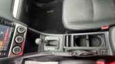 Interior of a car's front cabin showing the center console with gear shifter, climate controls, and a black leather seat nearby, viewed from above