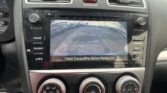 In-car infotainment screen showing a rearview camera feed with green, yellow, and red guide lines as the car backs up in a parking lot.
