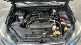 Open car hood showing the engine bay with various hoses, belts, and a visible yellow oil cap on the right side of the engine.