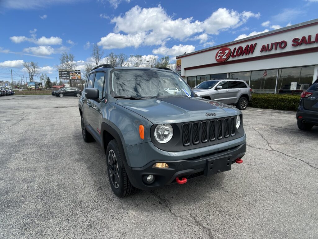 Front corner of a gray Jeep in a parking lot outside an auto dealership with an EZ Loan Auto Sales sign on the building behind.