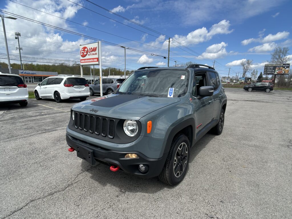 Front-right view of a gray Jeep in a dealership parking lot, with a prominent EZ LOAN Auto Sales sign and several parked cars nearby.