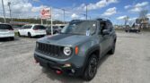 Front-right view of a gray Jeep in a dealership parking lot, with a prominent EZ LOAN Auto Sales sign and several parked cars nearby.