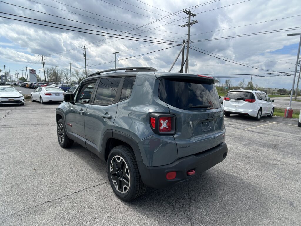Gray Jeep SUV seen from the rear quarter in a dealership parking lot with other cars around and cloudy sky overhead.