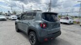 Gray Jeep SUV seen from the rear quarter in a dealership parking lot with other cars around and cloudy sky overhead.