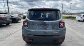 Rear view of a gray Jeep Wrangler Trailhawk in a parking lot, with other cars and a cloudy sky above.