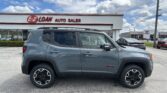 Gray Jeep Renegade SUV in foreground at an E-Z Loan Auto Sales lot under a blue sky with white clouds.